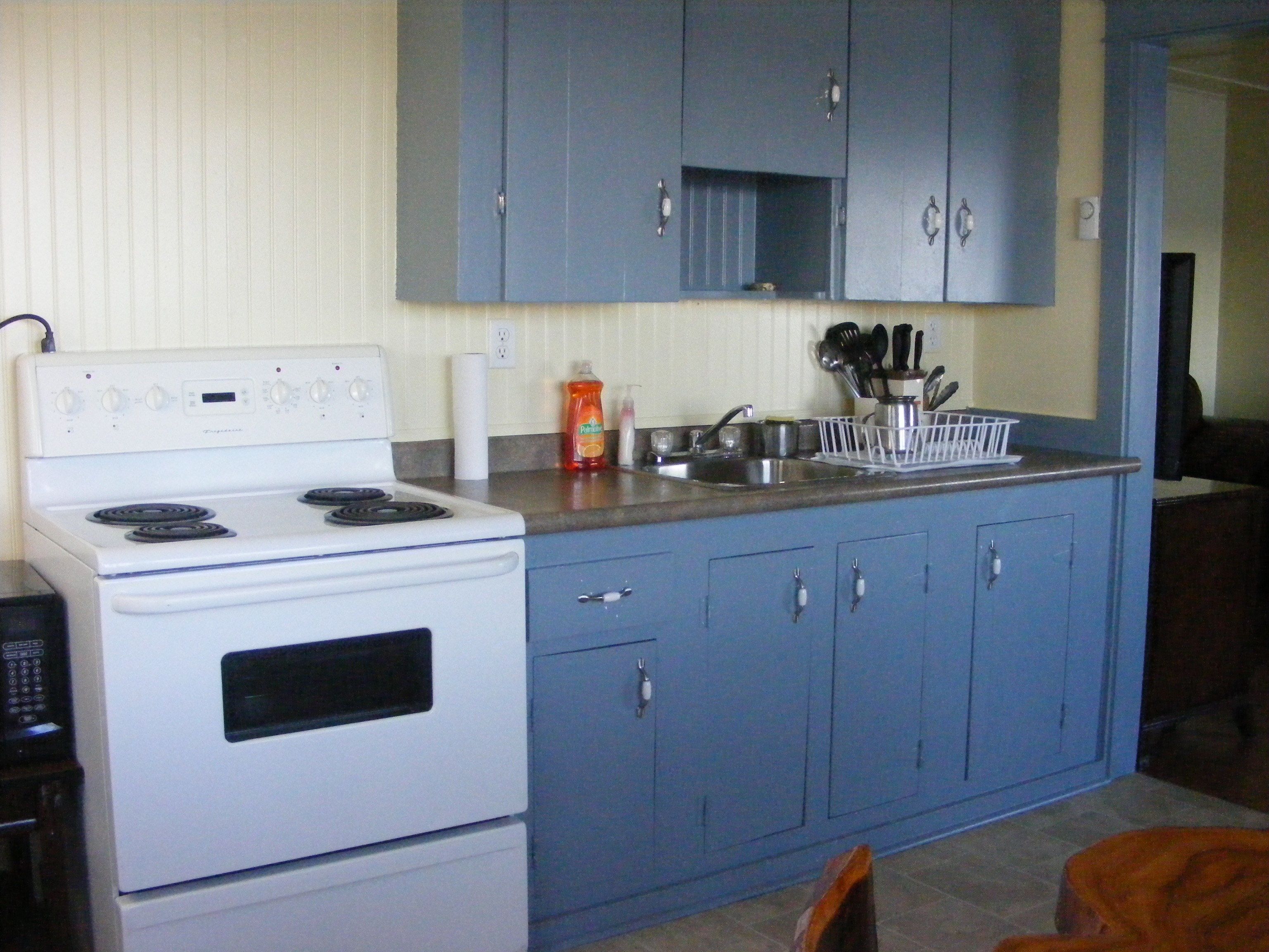 Una cocina compacta con estufa blanca, gabinetes azules y pileta de acero inoxidable.