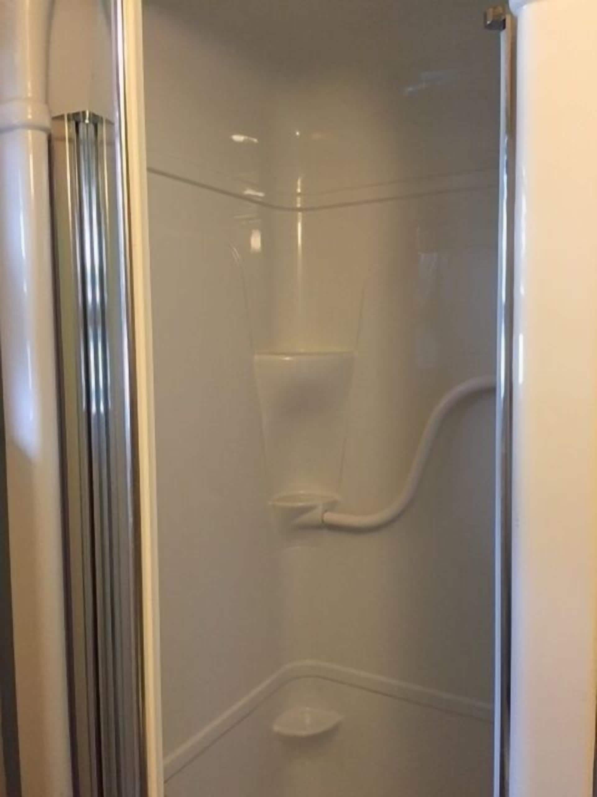 Een glazen douchecel met vrij uitzicht op het interieur, inclusief een douchekop en een klein plankje.