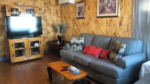 A wooden-paneled living room with a grey sofa, a wooden coffee table, a TV on a cabinet, and framed pictures on the wall. - Beautiful Seaside Cottage (Digby)