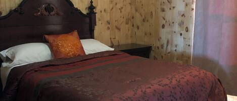 A wooden-paneled bedroom with a bed, a nightstand, and a window with a curtain.