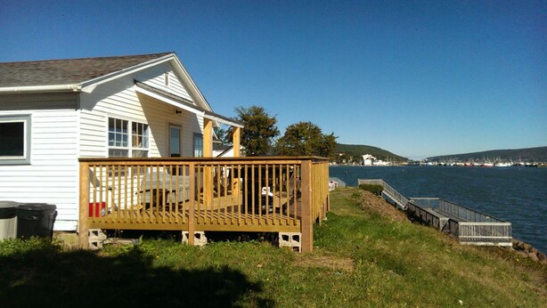 A white house with a wooden deck overlooking a body of water. - Beautiful Seaside Cottage (Digby)