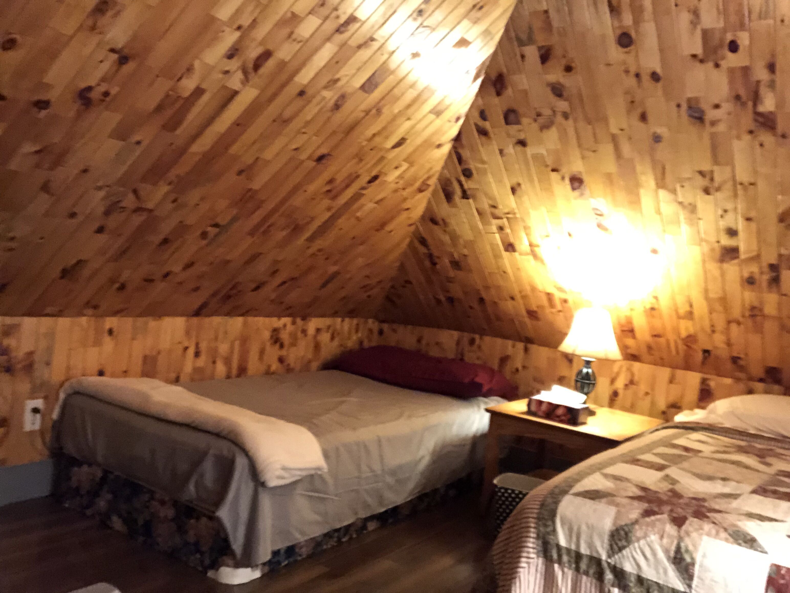 Une chambre mansardée chaleureuse avec des murs en bois, un lit avec un oreiller rouge et une table de chevet avec une lampe.