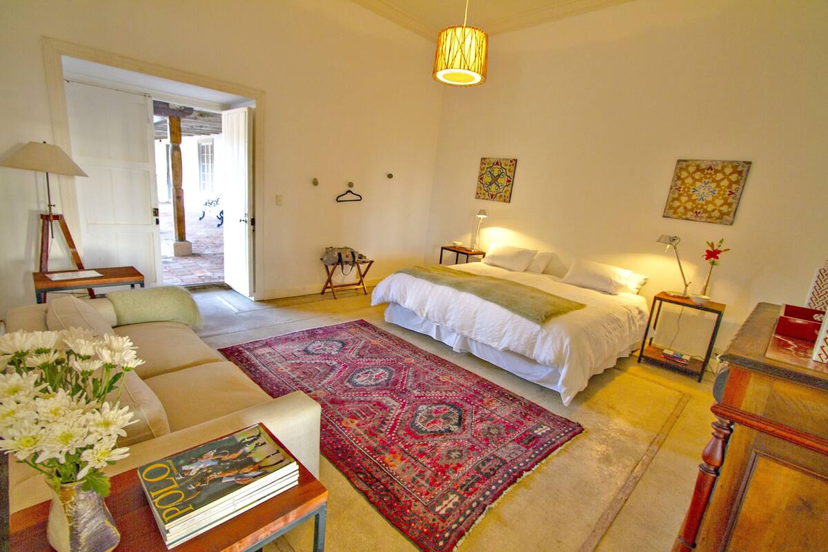 Ein Schlafzimmer mit einem Bett, einer Sitzecke inklusive Sofa und Couchtisch, einem Teppich und einer Lampe.