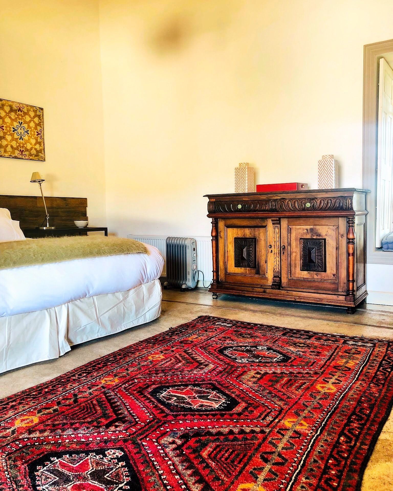 Un dormitorio con cama, un radiador, un armario de madera y un tapete estampado.