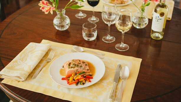 Une table à manger avec une assiette de saumon et de légumes, des verres à vin et une bouteille de vin.