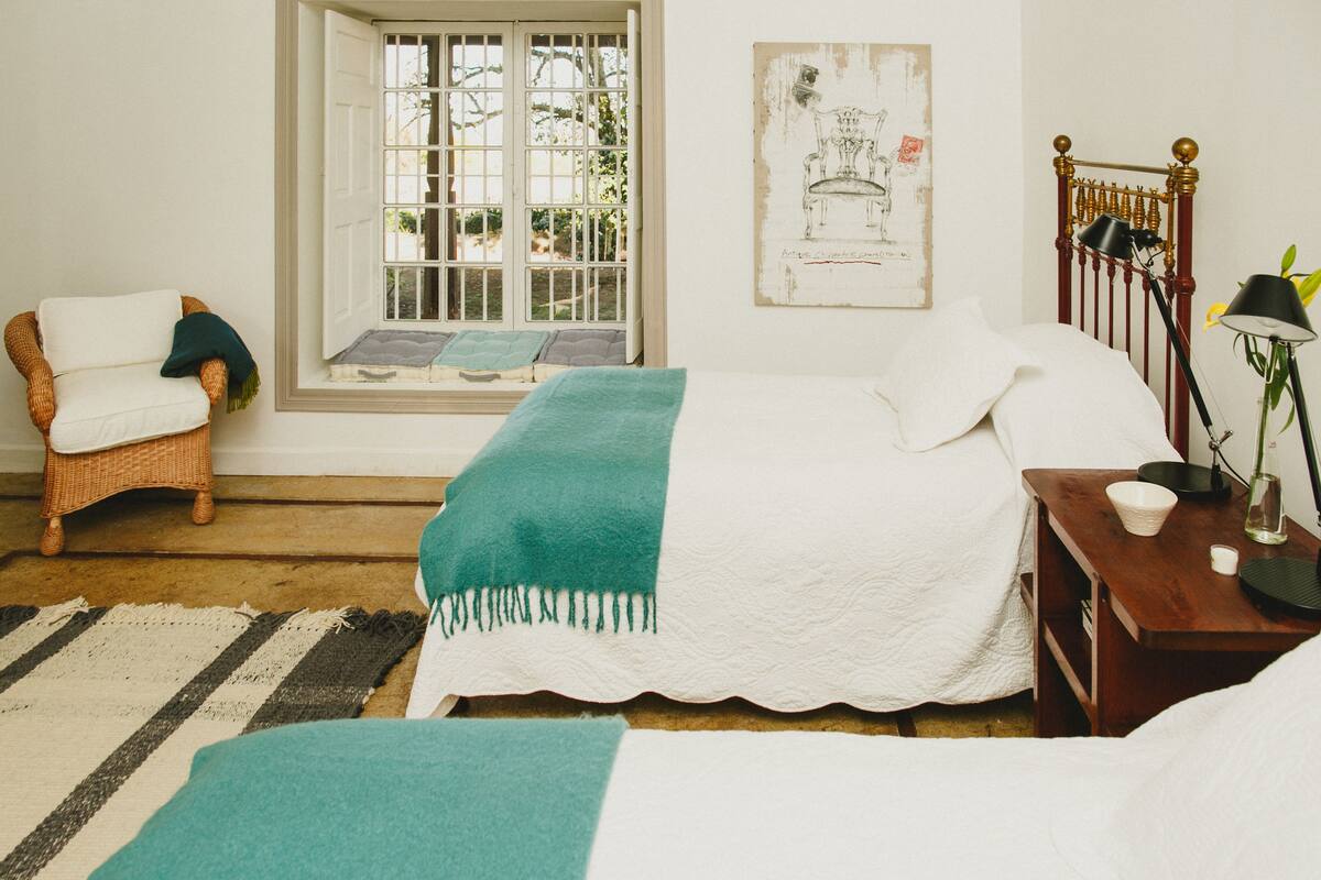 Ein Schlafzimmer mit einem Bett, einem Sessel, einem Fenster und einem Nachttisch.