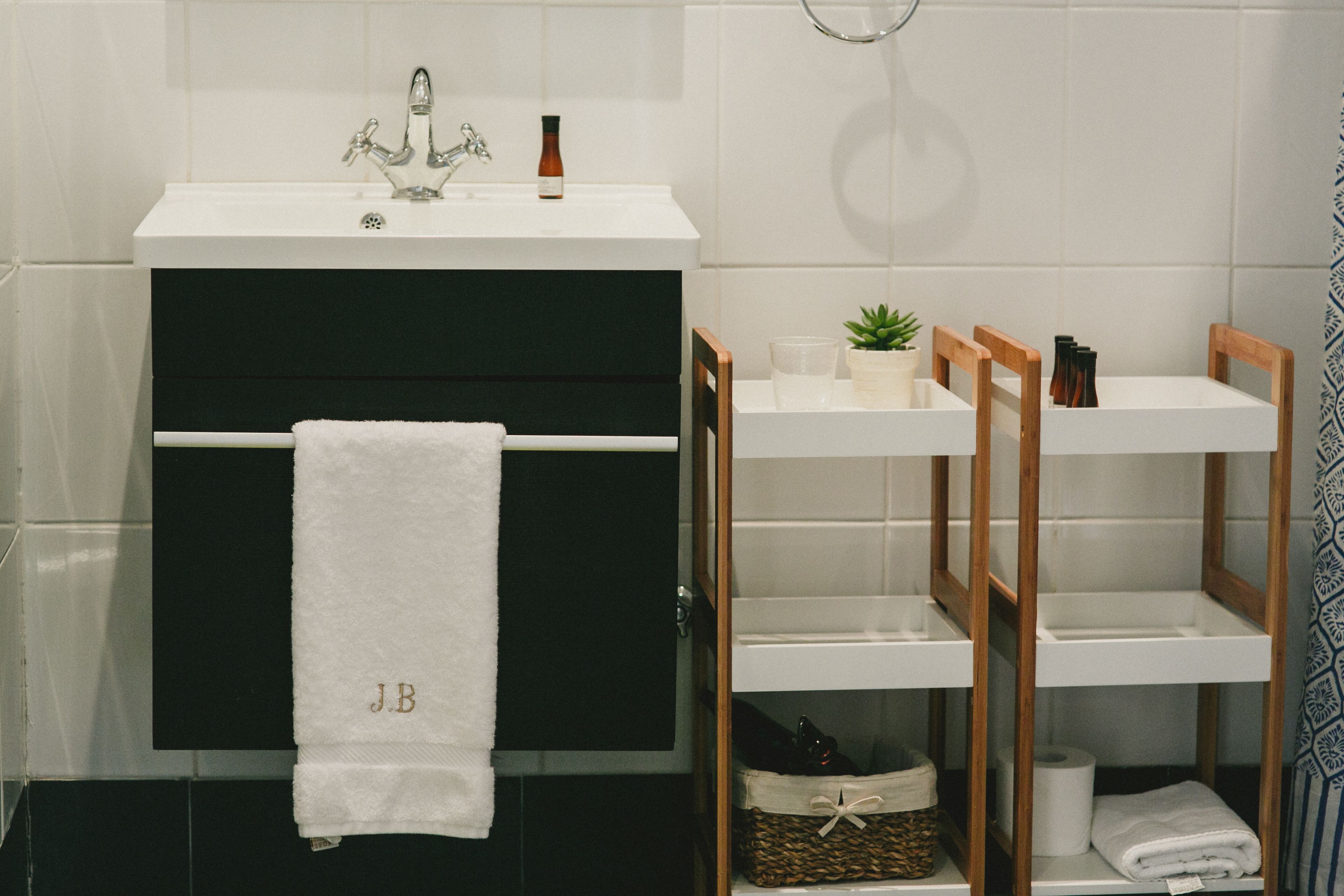 A bathroom with a white sink, a towel rack with a white towel, a small plant, and a shelf with toiletries.