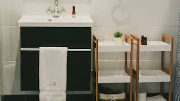 A bathroom with a white sink, a towel rack with a white towel, a small plant, and a shelf with toiletries.