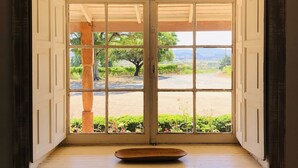 Quarto com uma grande janela, piso de madeira e uma pequena mesa de madeira.