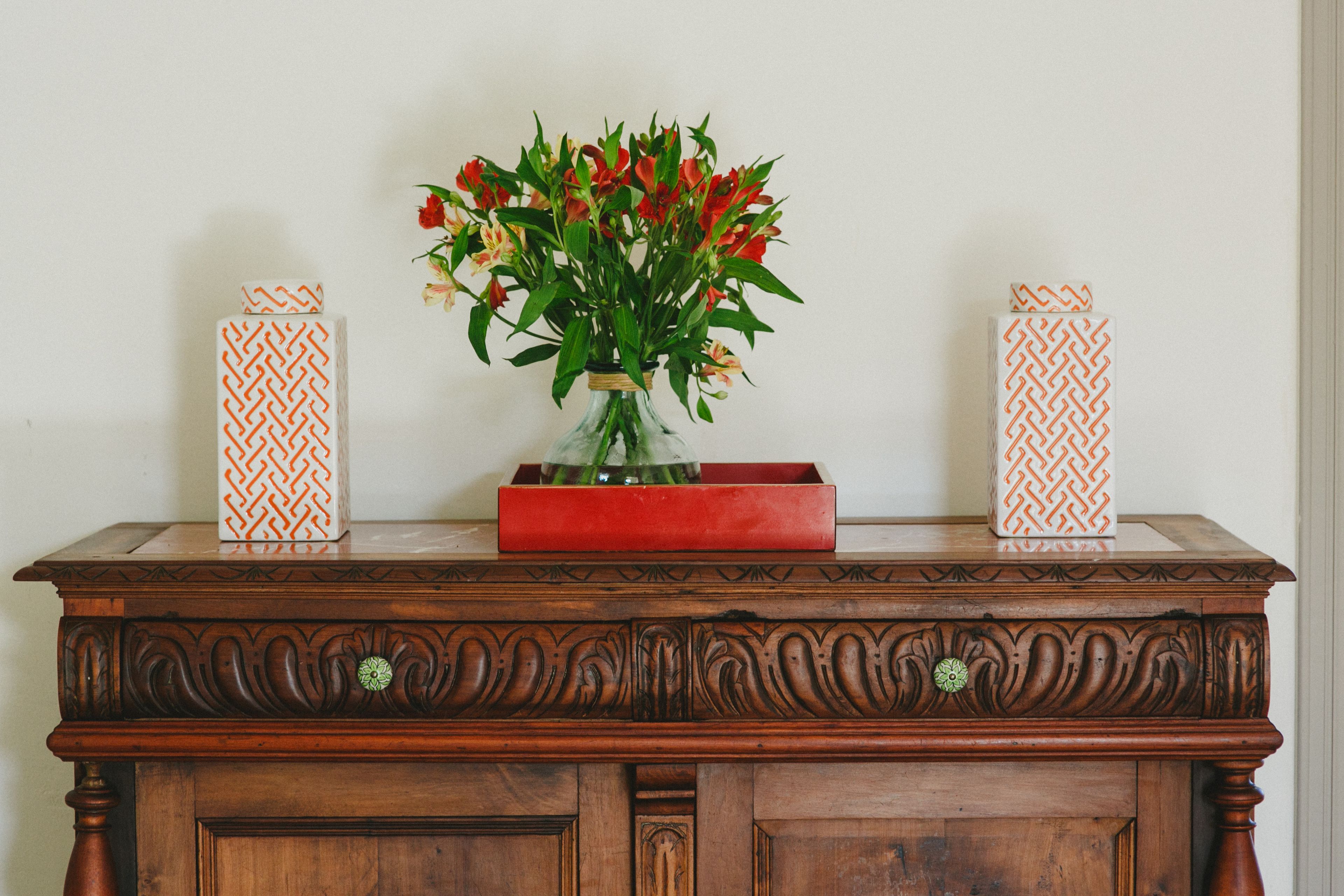 Eine Holzkommode mit einer Blumenvase und zwei verzierten Kisten darauf.