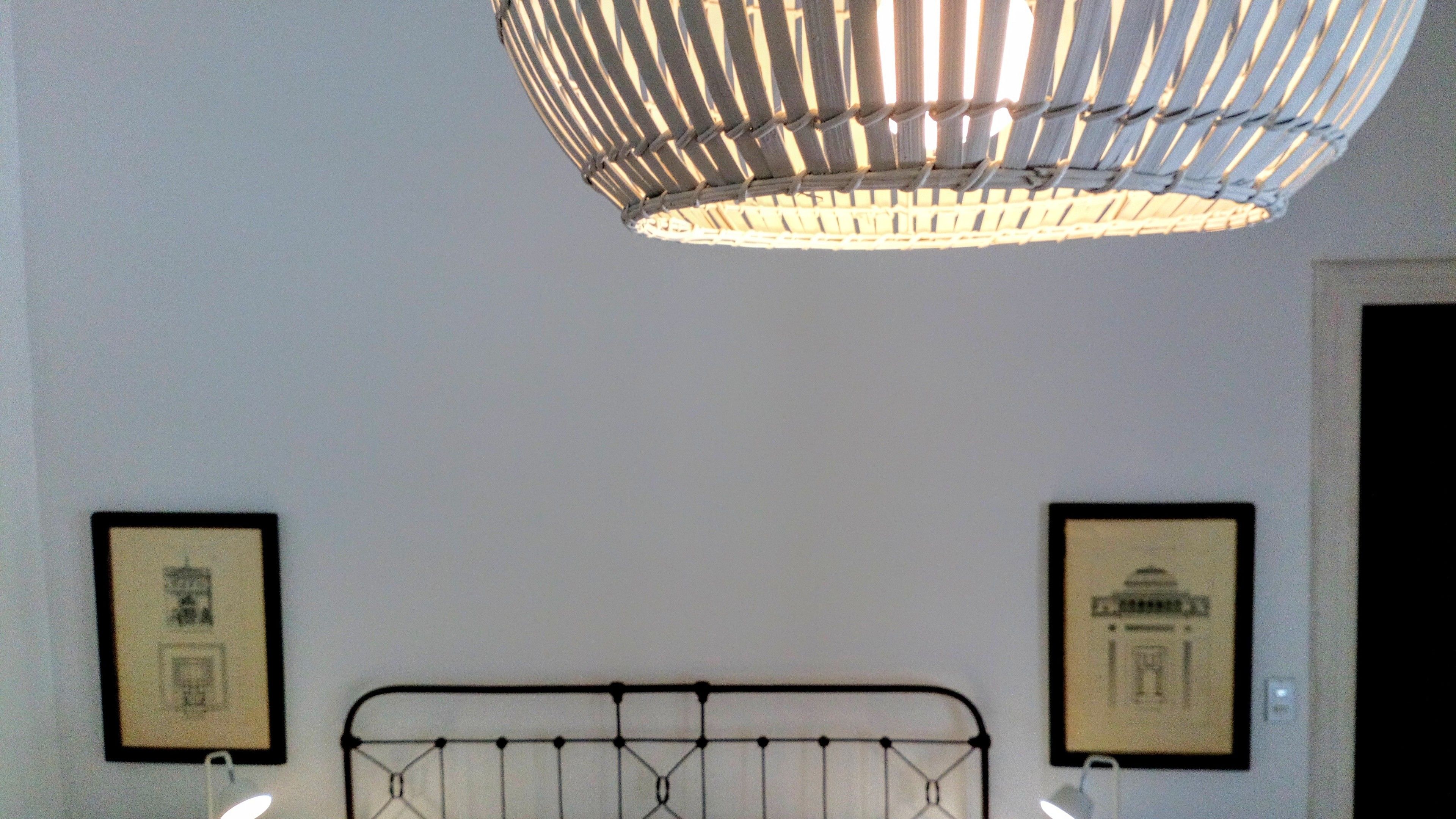 A room with a metal bed frame, a hanging light fixture, and two framed pictures on the wall.