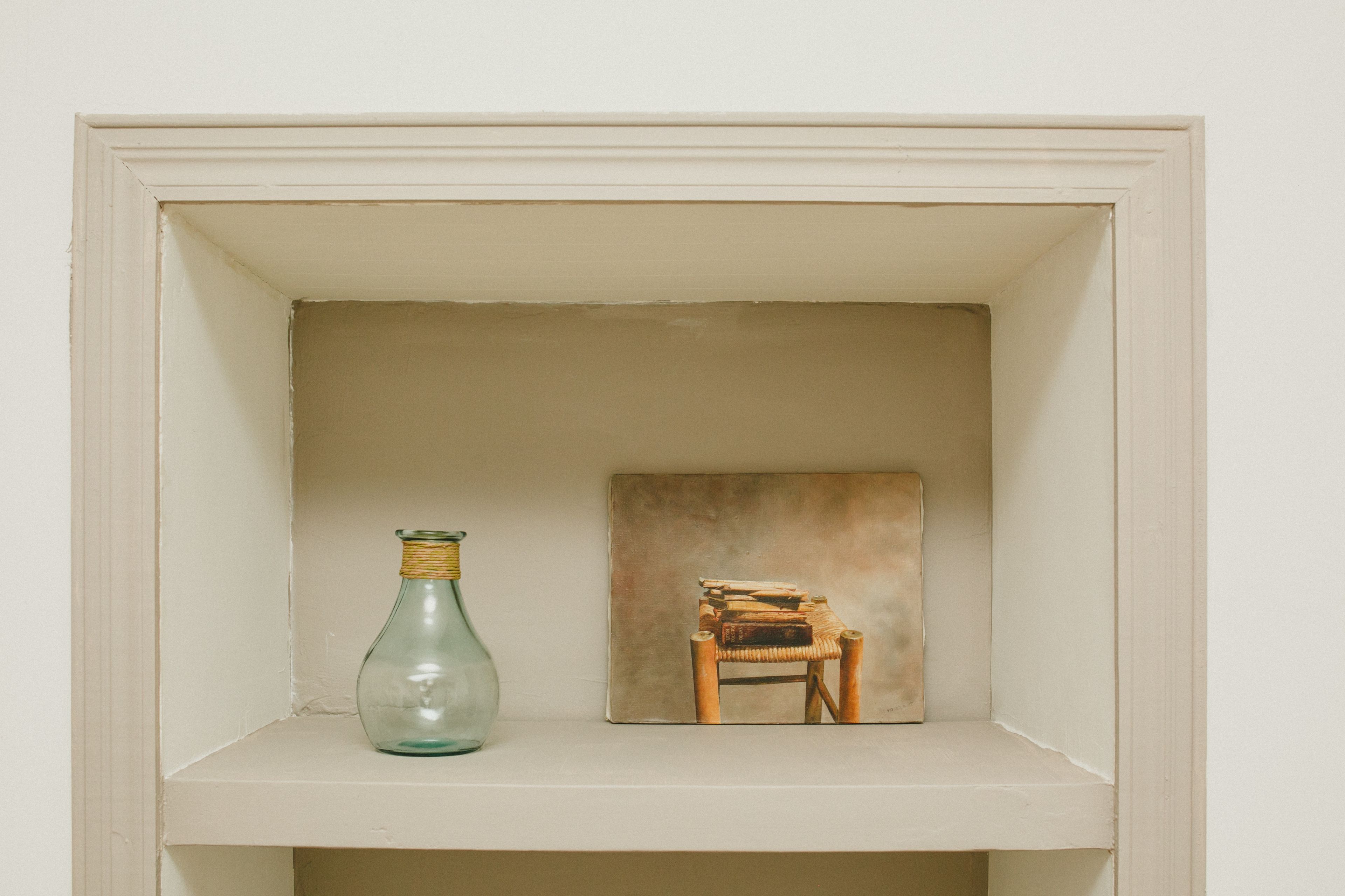 A shelf with a glass bottle and a small wooden chair.
