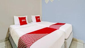 Habitación de hotel con cama, dos almohadas con la marca 'OYO', una manta roja y blanca estampada, y una pared azul claro con diseño geométrico.
