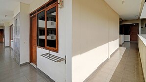 Un pasillo con una puerta de madera, una ventana con un tendedero de metal y un suelo de baldosas.