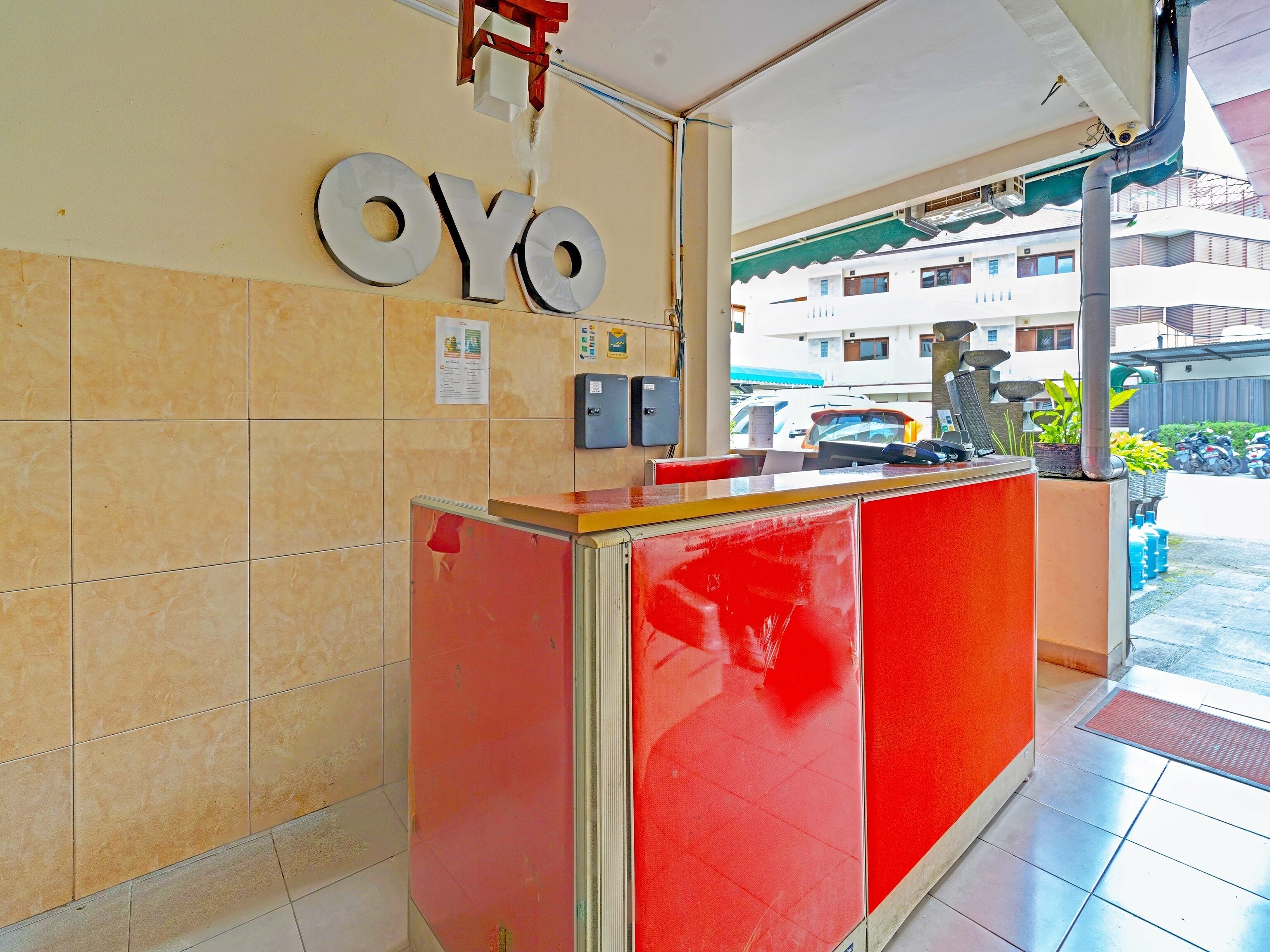 A reception desk with a red and beige color scheme, a sign reading "OYO", and a view of the street outside.