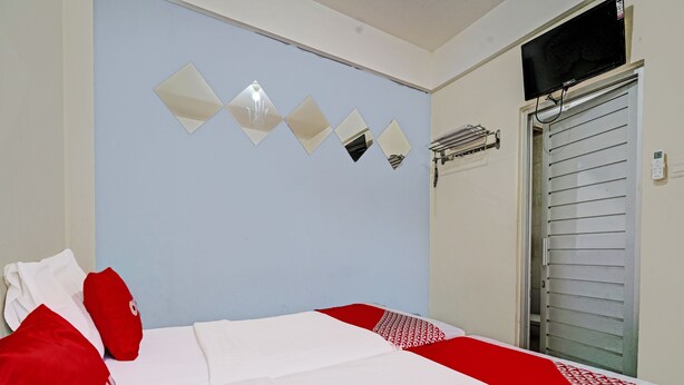 A bedroom with a bed, pillows, a wall-mounted mirror, and a window with blinds. - OYO 1699 Verona Residence (Bandung)