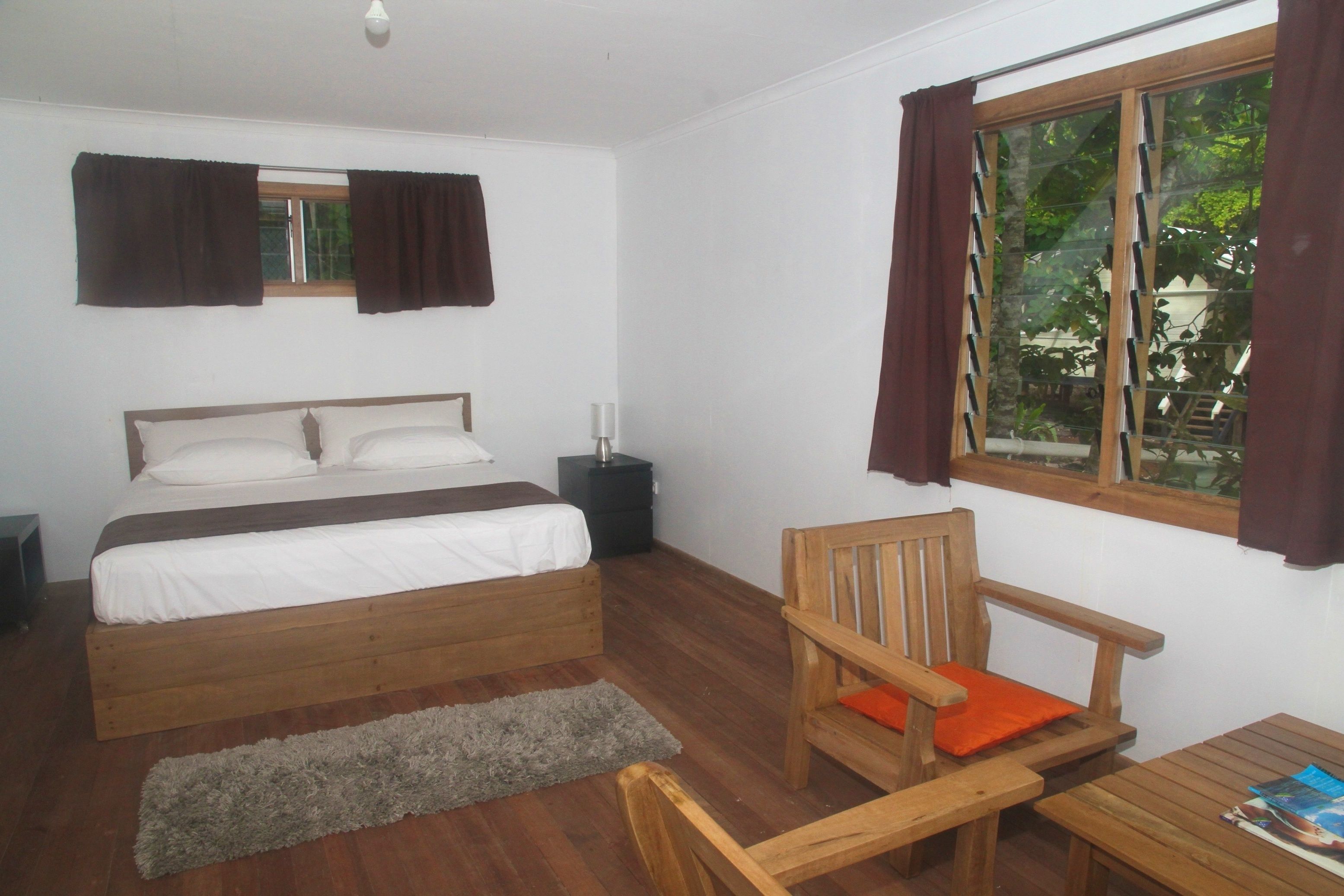 A bedroom with a bed, wooden chair, table, and window with curtains.