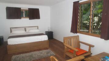 A bedroom with a bed, wooden chair, table, and window with curtains.