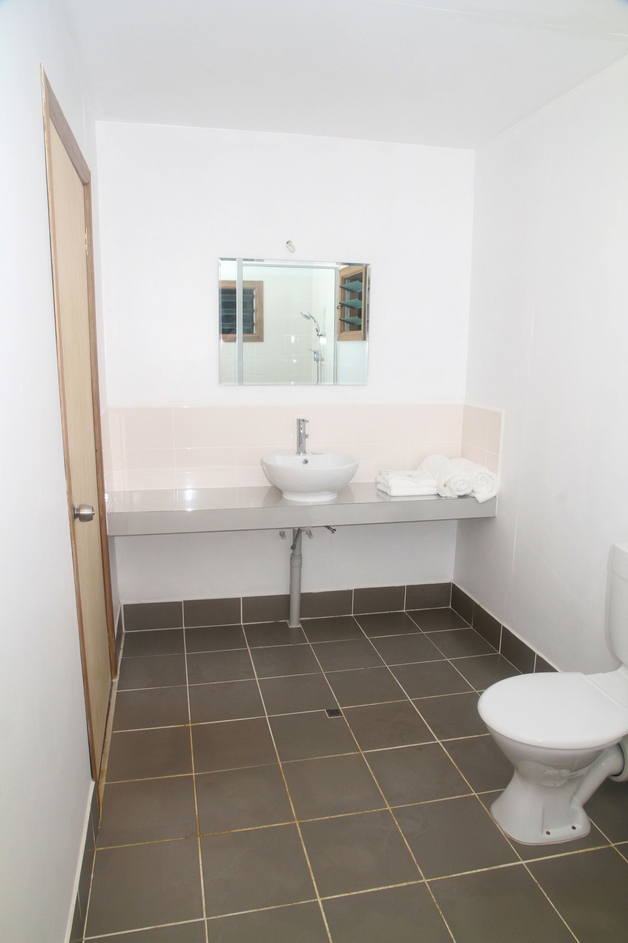 A small bathroom with a white sink, a mirror above it, a toilet, and a door.