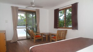 Una habitación con una cama, una mesa de madera, dos sillas, un ventanal con cortinas y vista a un cuerpo de agua.