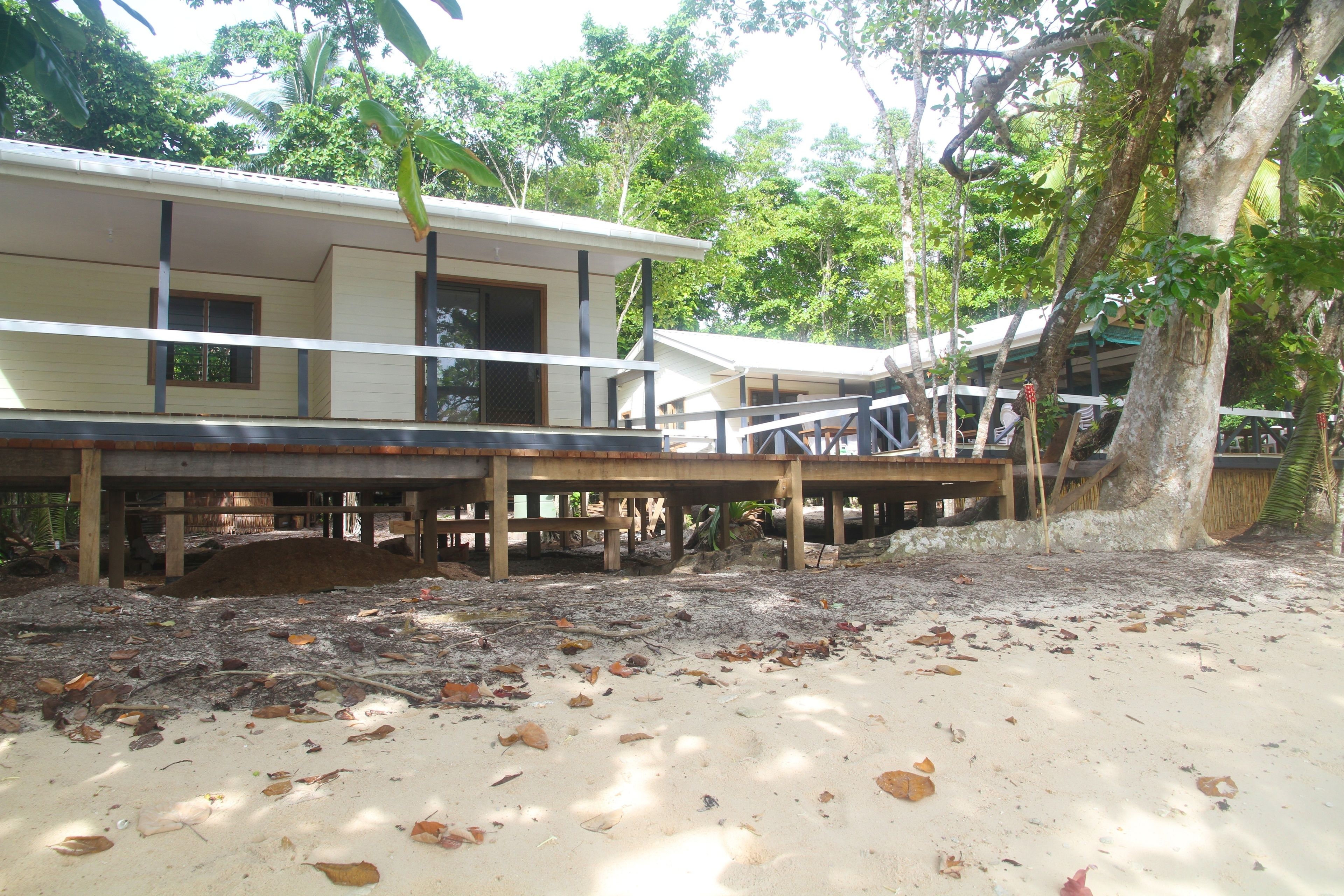 Une propriété située en bord de mer, dotée d’une terrasse en bois, d’un espace couvert et d’un bâtiment comprenant plusieurs pièces.
