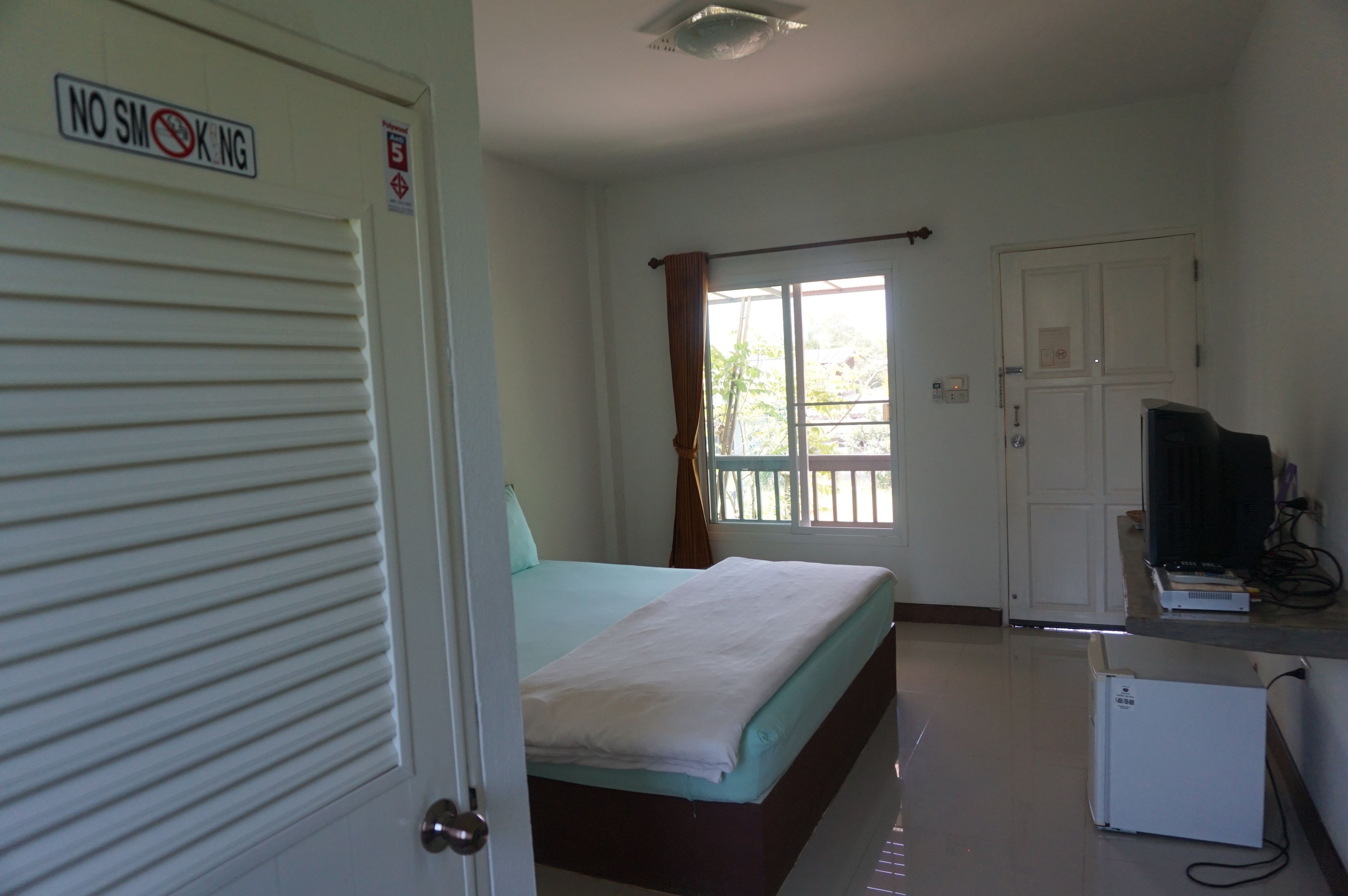 A bedroom with a bed, a TV, a desk, and a door with a 'No Smoking' sign.