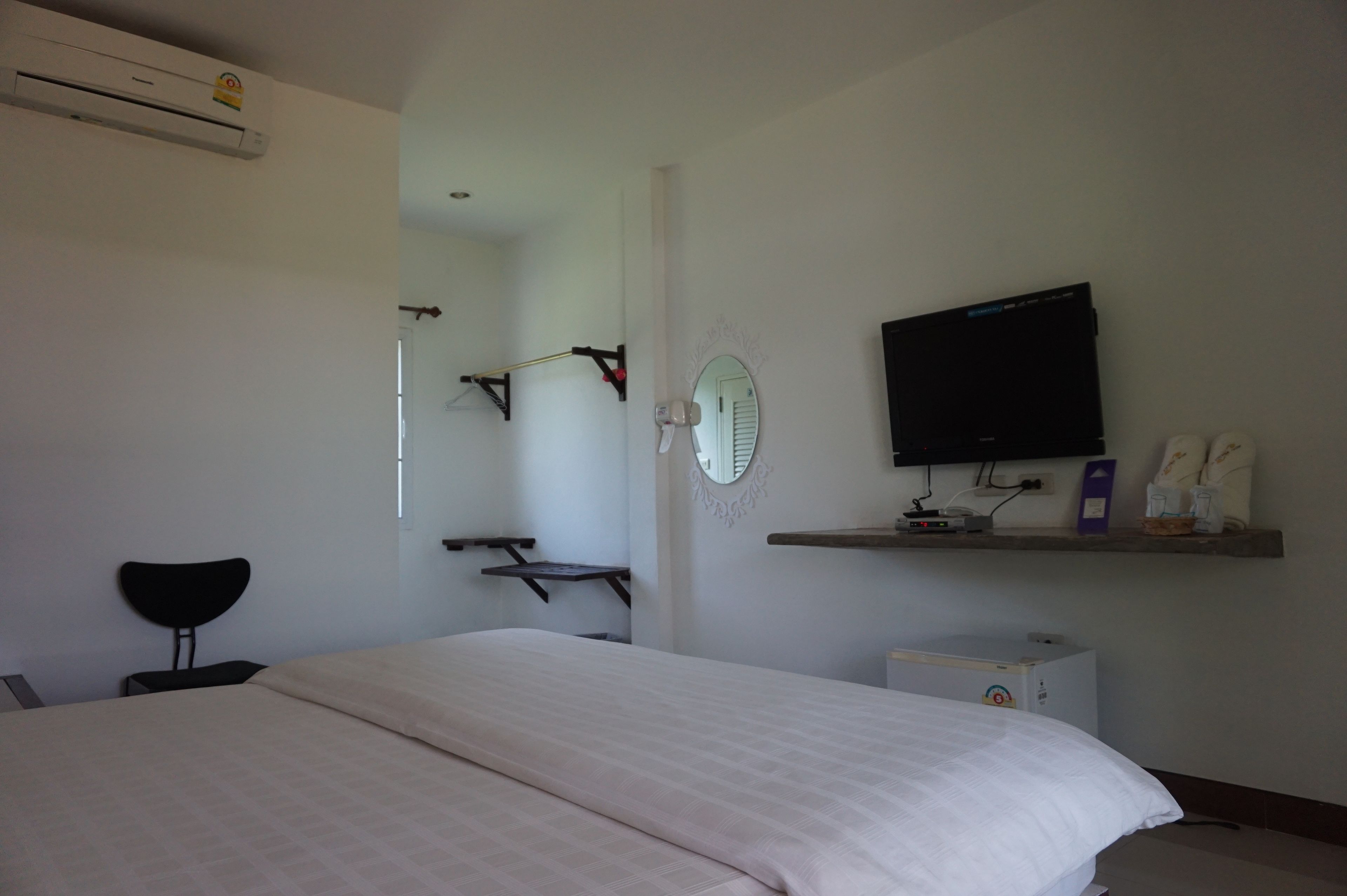 A bedroom with a bed, a TV, a small cabinet, and a chair.