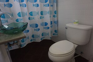 A bathroom with a toilet, a glass basin sink, and a shower curtain with a fish pattern.