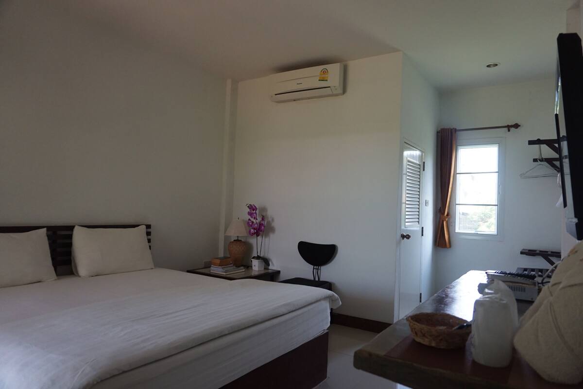 A hotel room with a bed, bedside table, lamp, and an air conditioning unit.