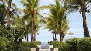 A pathway leading to a beach with palm trees and a view of the ocean.