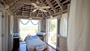A room with a bed, a ceiling fan, and a view of the beach.