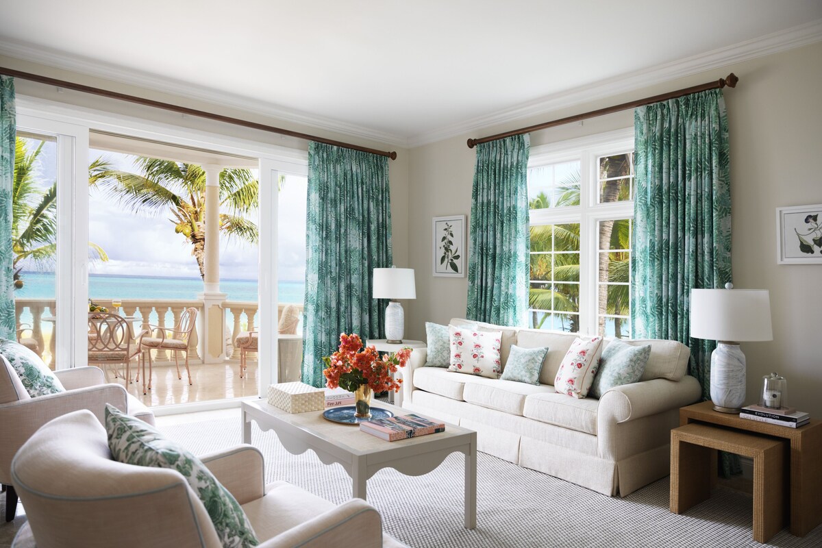 A spacious living room with a balcony, white furniture, and green curtains.