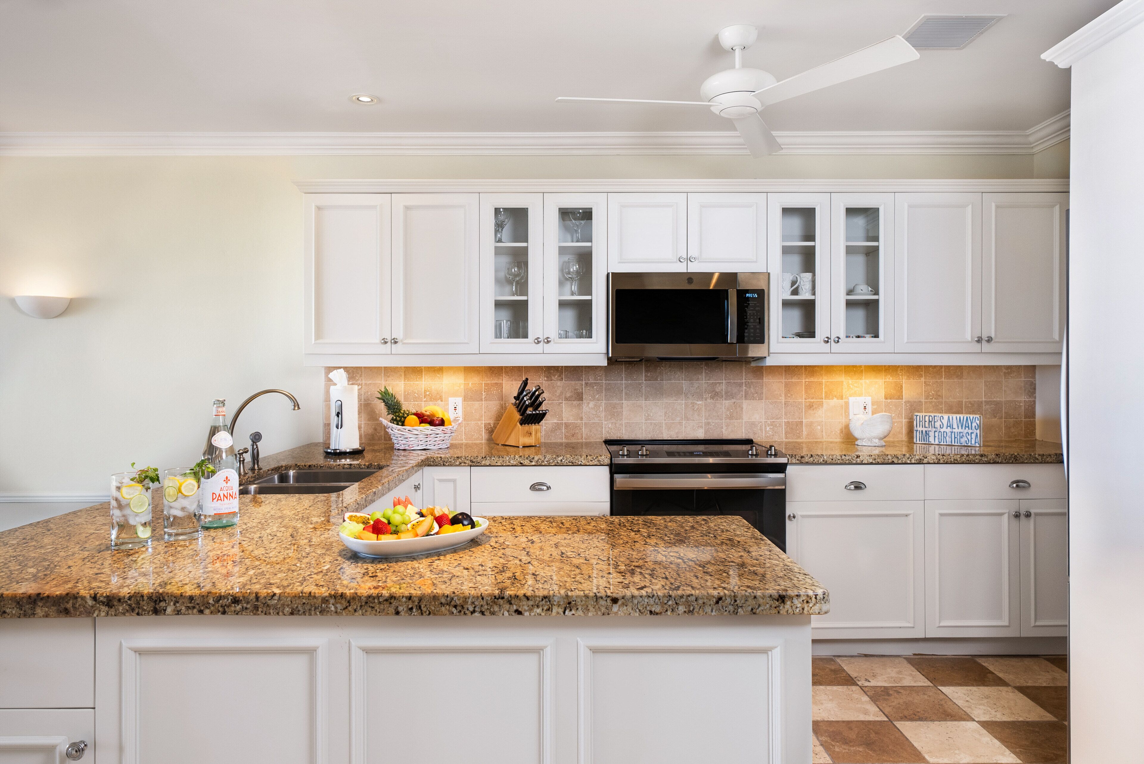 A kitchen with white cabinets, a granite countertop, a stainless steel microwave, and a ceiling fan.