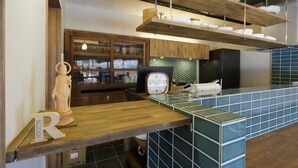 A kitchen with wooden cabinets, a clock, and a tiled backsplash. - NARA Guesthouse KAMUNABI - Hostel (Nara)
