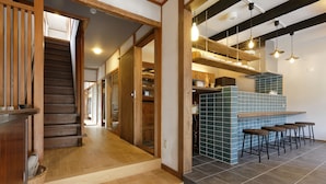 A modern kitchen with a bar area, wooden staircase, and a view into the dining area. - NARA Guesthouse KAMUNABI - Hostel (Nara)