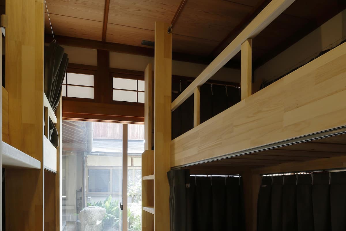 A room with a wooden floor, bunk beds, and a sliding door leading to an outdoor area with plants.