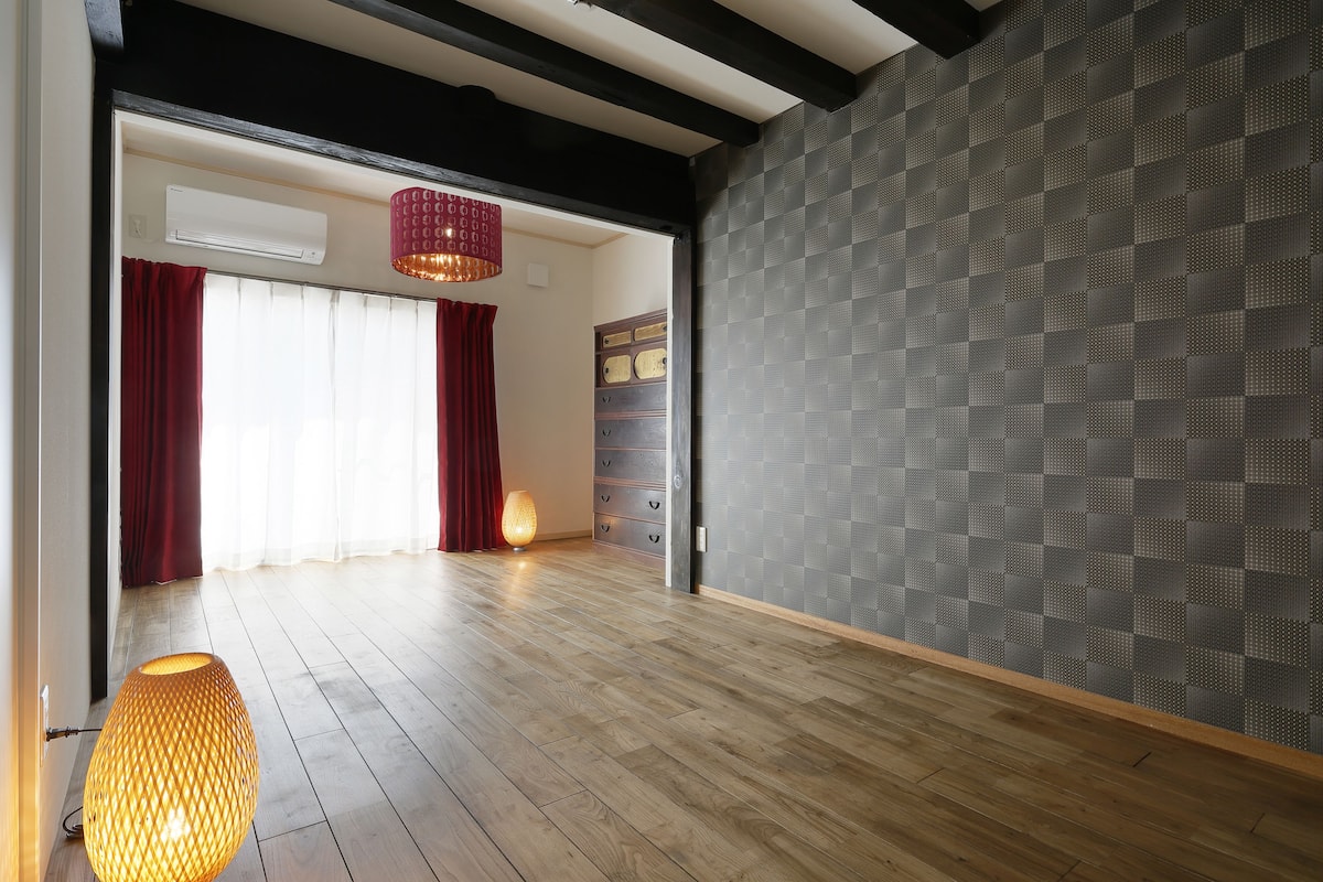 A spacious room with wooden flooring, a patterned wall, and a large window with curtains.