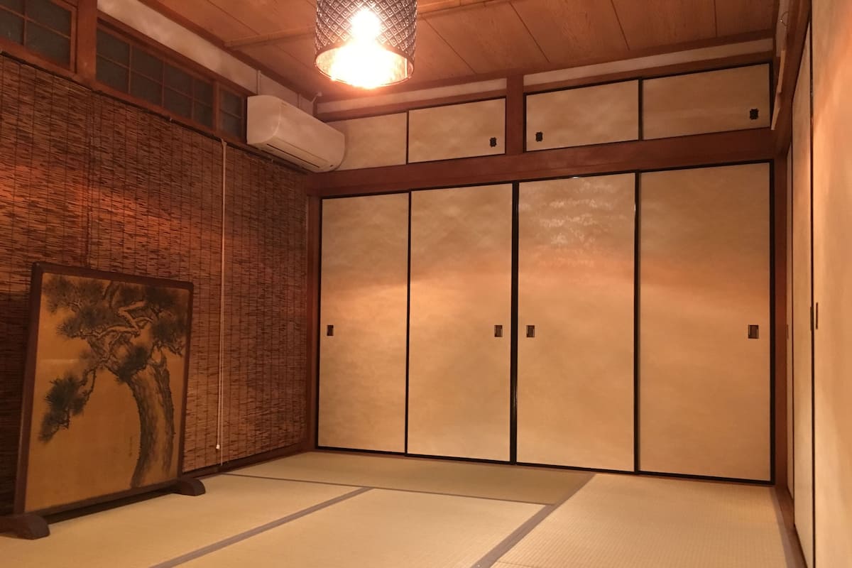 A traditional Japanese room with tatami flooring, a shoji screen, and a hanging light fixture.