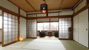 A traditional Japanese room with tatami flooring, sliding doors, a hanging light fixture, and a view through the shoji screen. - NARA Guesthouse KAMUNABI - Hostel (Nara)