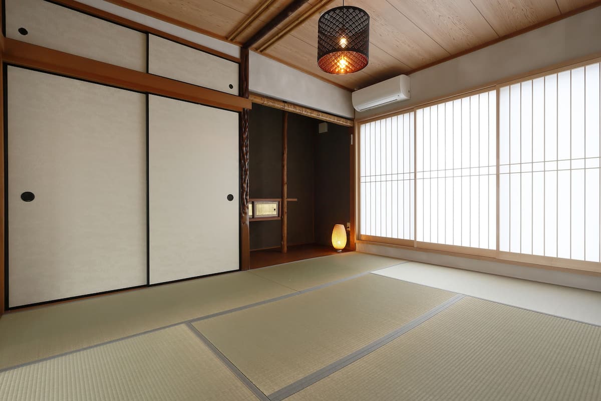 A traditional Japanese room with tatami flooring, sliding doors, and a hanging light fixture.