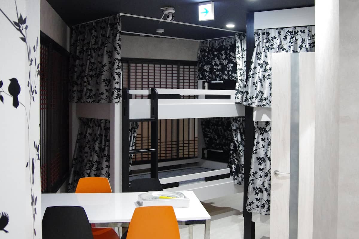 Una habitación con literas, una mesa de comedor con sillas y un televisor pequeño en el techo.