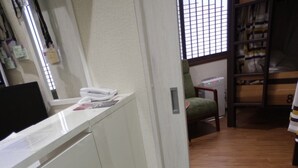 A narrow hallway with a wooden floor, a white desk, a chair, and a bunk bed in the background.