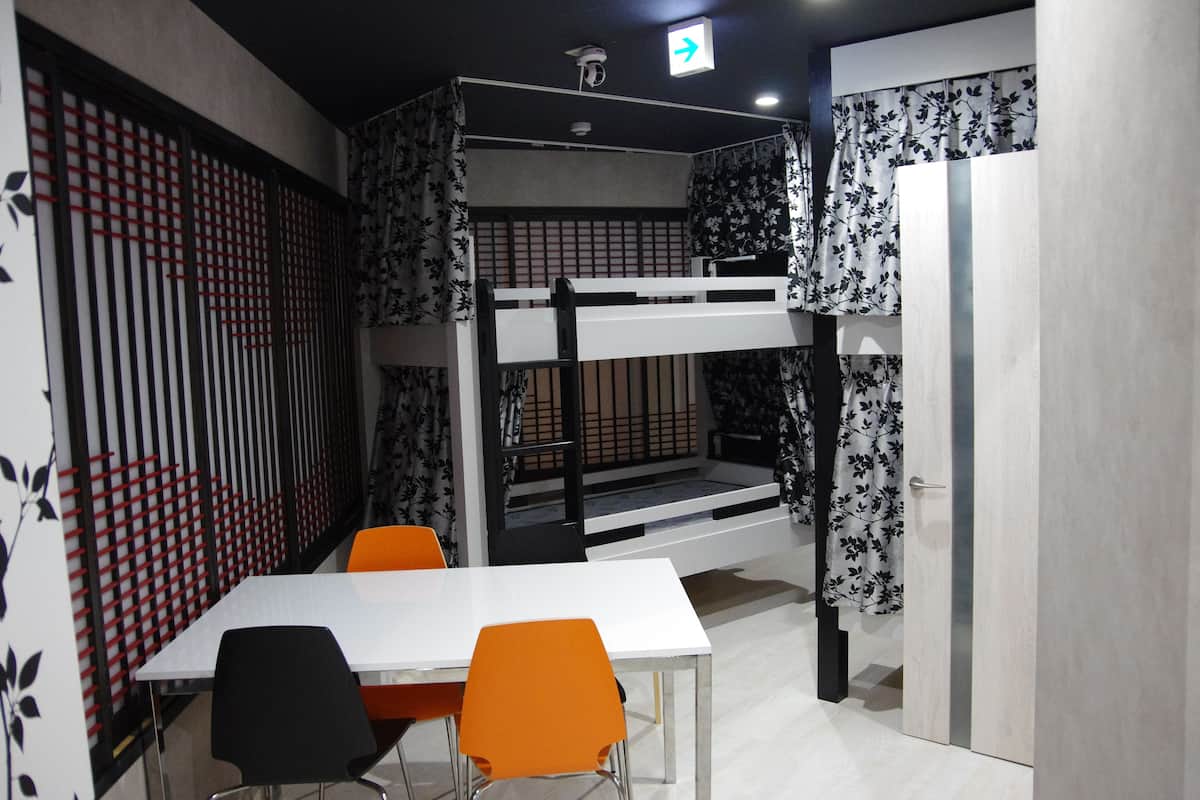 Una cama litera con diseño blanco y negro, una mesa blanca con dos sillas y una cortina estampada.