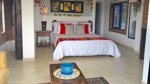 A bedroom with a bed, a nightstand, a blue bowl on a table, and a decorative wall piece. - Mamatina Hotel (Santa Rosa de Cabal)