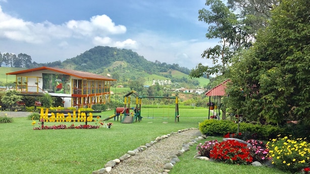 A playground with swings and slides, surrounded by a garden with colorful flowers and a path. - Mamatina Hotel (Santa Rosa de Cabal)