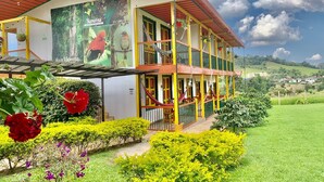A two-story building with a balcony, surrounded by well-maintained gardens and a clear view of the countryside. - Mamatina Hotel (Santa Rosa de Cabal)