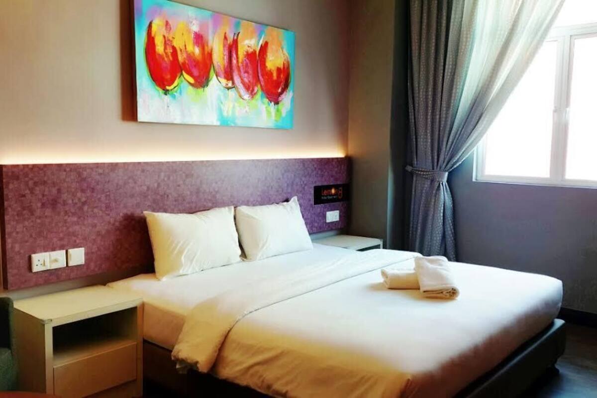 Une chambre d’hôtel avec un grand lit, une tête de lit dotée d’un panneau de commande, une table de chevet et une peinture abstraite aux couleurs vives accrochée au mur.