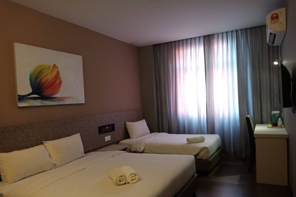 Une chambre d’hôtel avec deux lits, un bureau, une chaise, un tableau et une fenêtre avec des rideaux.