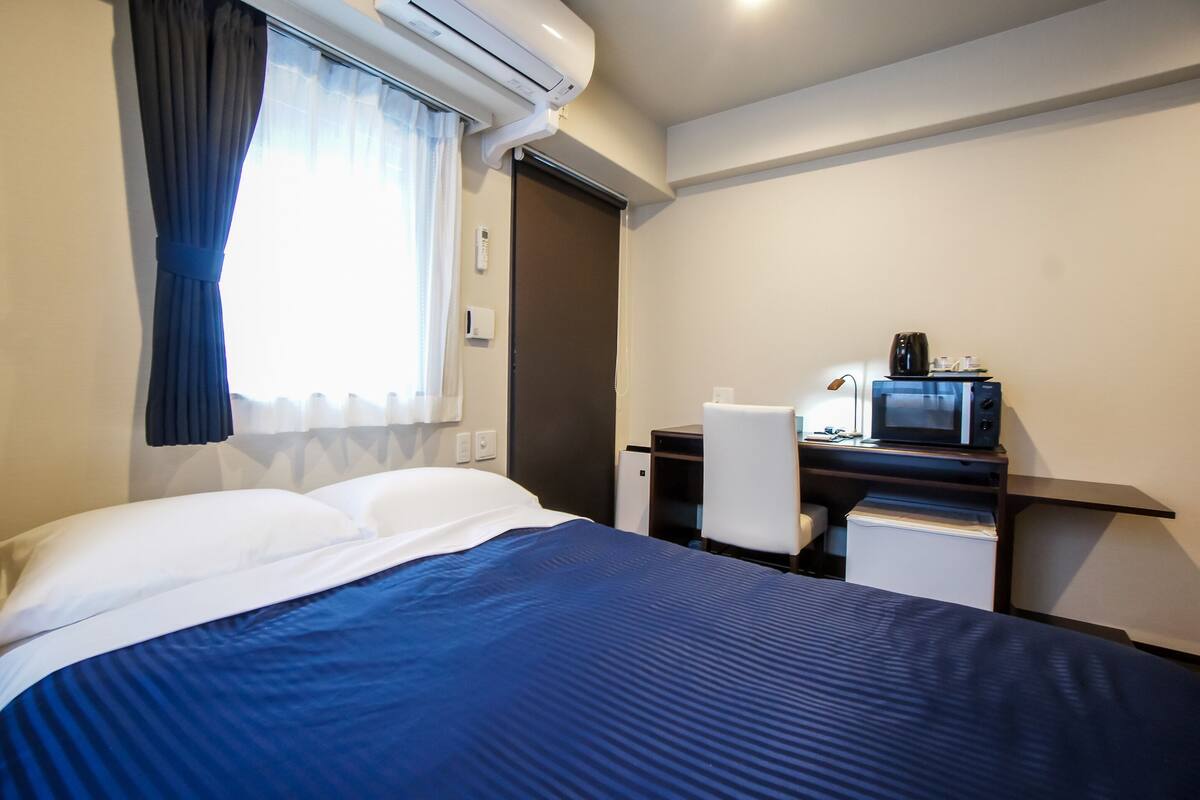 A hotel room with a bed, a desk with a computer, a microwave, and a chair.