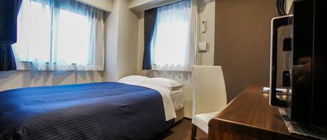 Quarto de hotel com uma cama, uma mesa com cafeteira e duas janelas com cortinas.